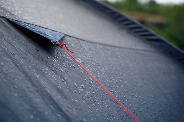 Yakından bakınca, yağmur damlalarıyla kaplı koyu mavi su geçirmez çadır üzerindeki kırmızı halatı çapalamanın ayrıntılı görüntüsü.