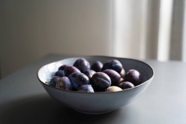 Taze olgun erik meyvelerinin manzarası zarif gri kasede, masa içinde, doğal ışık ile minimalist bir düzende.