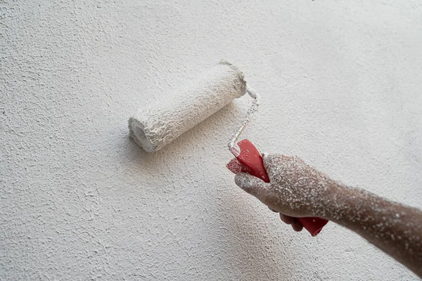 front view closeup of Caucasian male hand full of dirt painting an exterior wall and renovating with white color paint roller