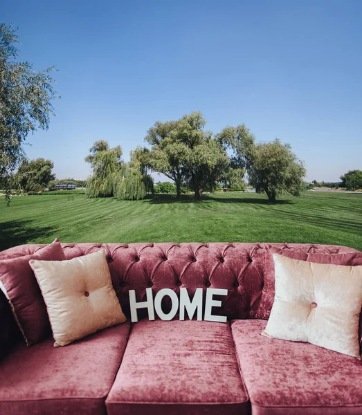 Collage with sofa, home and landscape with green lawn. Concept. Soft comfortable sofa. Hygge. Home. Pink sofa made of velor.