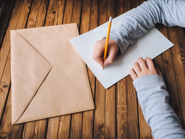 Children hands writing letter. Brown envelope, white sheet of paper and pencil.