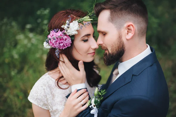 Bride with wreath of real flowers gently embracing with bearded groom.