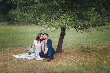 Portre çim ağacın altında oturan yeni evliler sevgi dolu. Gelin düğün buket holding.