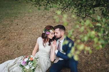 Portre çim ağacın altında oturan yeni evliler sevgi dolu. Gelin düğün buket holding.