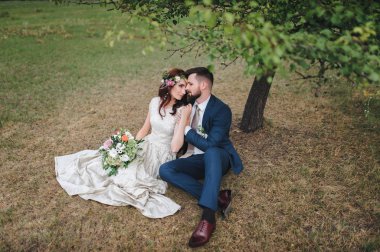 Portre çim ağacın altında oturan yeni evliler sevgi dolu. Gelin düğün buket holding.