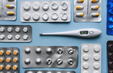 Elektronik termometre üzerinde bulunmakta - çetele gribi üzerinden. Blister paketleri mavi zemin üzerine hap. Nezle ve tedavisi kavramı. Geleneksel tıp. 