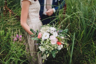 Gelinin ellerinde düğün buketi. Gelin ve damat yeşil çim. Güzel sanat tarzı.