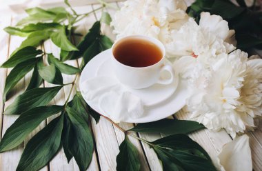 Yeşil çay ve beyaz taze peonies ışık gri ahşap arka plan üzerinde beyaz porselen fincan. Üstten Görünüm, öğle yemeği molası kavramı.