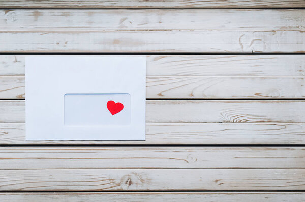 Белый конверт с любовным письмом ко Дню Святого Валентина. Красное сердце в белом конверте. Деревянный фон
.