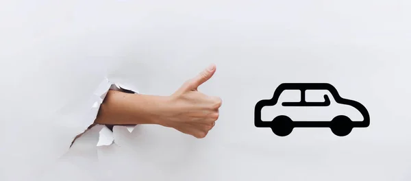 Hand with a raised thumb near the symbol of car. The concept of driving school, loan, mortgage, excellent quality automotive industry. Like, cool, good. ?lick like.