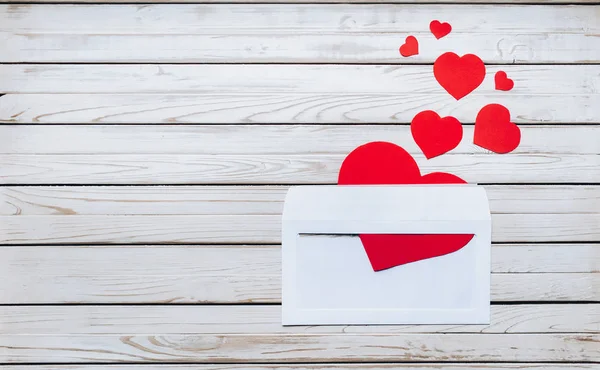 White envelope with a love letter for St. Valentine\'s Day. Red hearts in a white envelope. Wooden background.