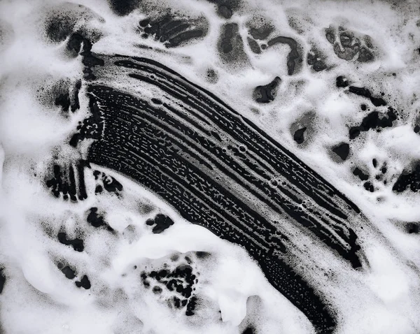 White foam and soap on dark background. Abstract pattern. The concept of washing oily pan or black car. Guest worker,