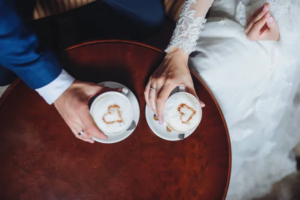 一杯のコーヒーのための美しいカフェに座っている新婚者のカップル カプチーノの泡と白いカップは 心のシンボル — ストック写真