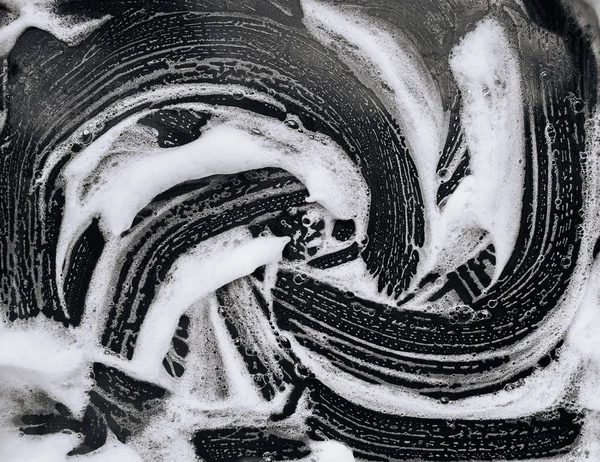 Foam and soap on dark background. Abstract pattern. The concept of washing oily pan or black car. Guest worker,