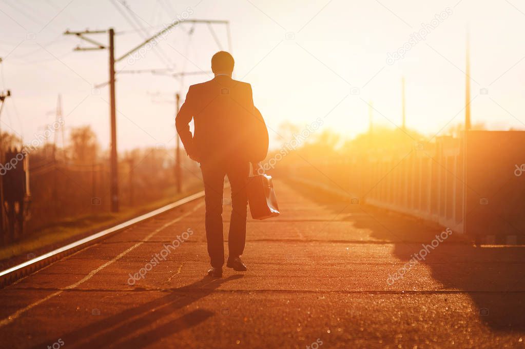 Businessman in suit with suitcase walking on road to meet sunrise. The way of the businessman.