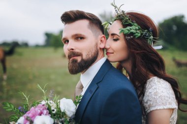 Onu şefkatle kucaklayan gelin damat ve onu boynundan öper. Bir gelin buketi ve başında gerçek çiçek çelenk.