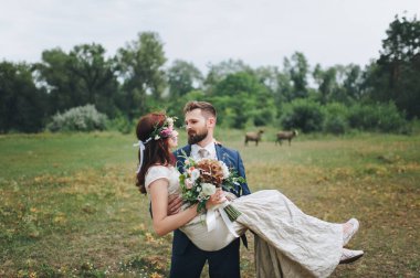 Damat gelini kollarını kaldırdı. Gelin buketi ve taze çiçek çelenk ile.