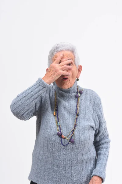 Senior vrouw gluren met hand op gezicht op witte achtergrond — Stockfoto