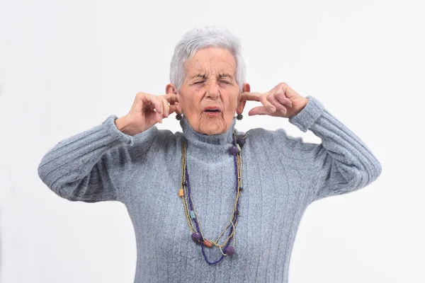 Mujer mayor haciendo ruido lastimando sus oídos sobre fondo blanco —  Fotos de Stock