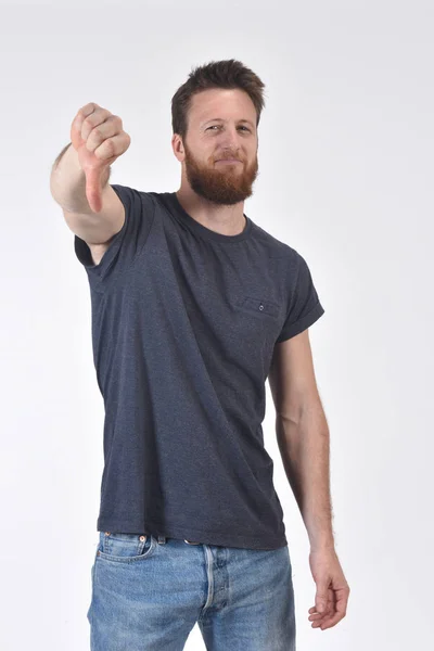 Homem segurando seu polegar para baixo e sério no fundo branco — Fotografia de Stock