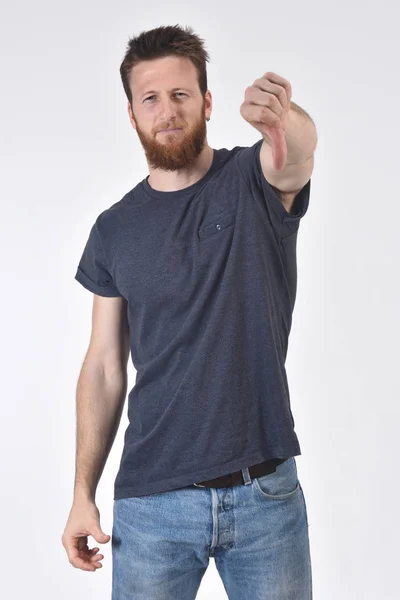 Hombre sosteniendo su pulgar hacia abajo y serio sobre fondo blanco, seri — Foto de Stock