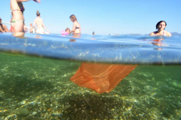 Gente en la playa y basura plástica flotando —  Fotos de Stock