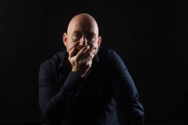 Adam kameraya bakıyor ve eli çenesinde, arka planda.