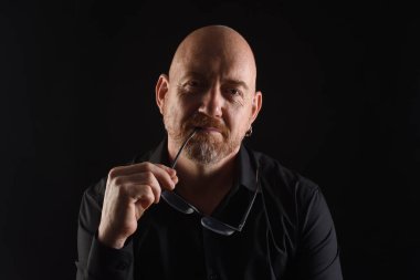 Siyah arka planda göz takan bir adamın portresi.