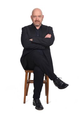 Beyaz arka planda oturan kolları ve bacakları çaprazlanmış kel adam.