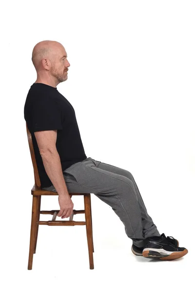 Beyaz arka planda sandalyede oturan kel bir adam..