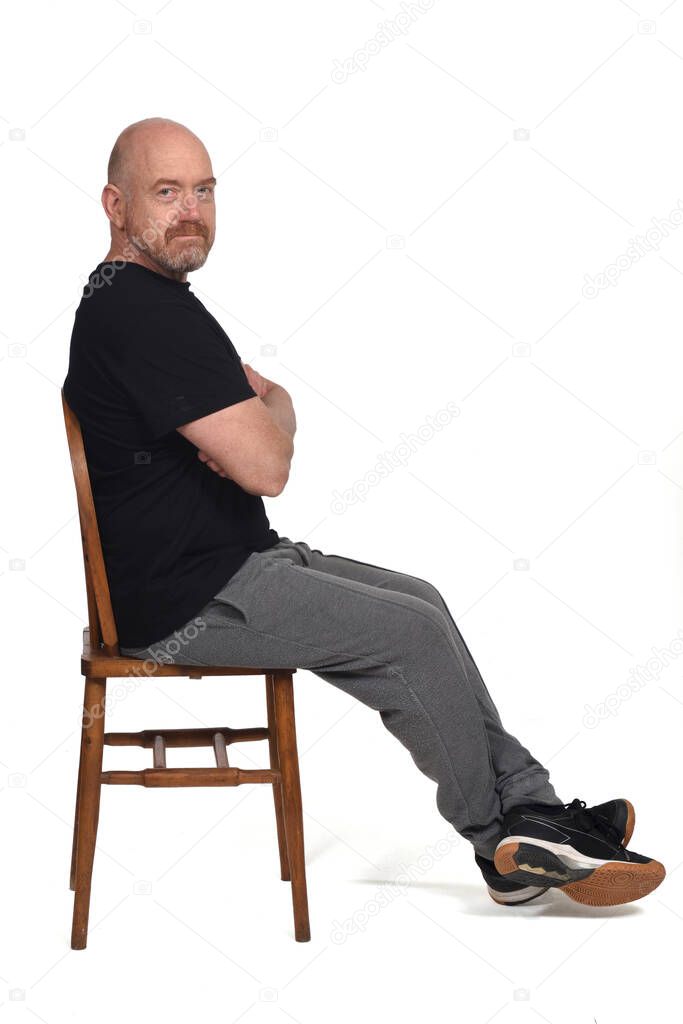 Bald man with sportswear sitting on a chair on white background, looking at camera