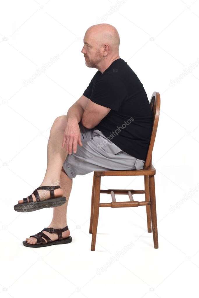 Bald man with sandals t-shirt and shorts sitting on white background, side view,