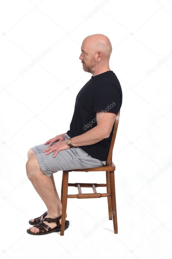 Bald man with sandals t-shirt and shorts sitting on white background, look side