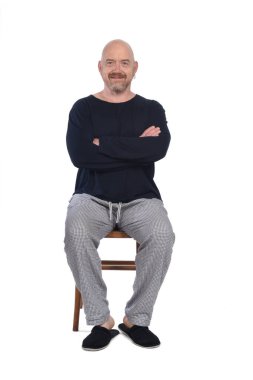 Beyaz arka planda sandalyede oturan pijamalı adam, kollarını kavuşturdu.