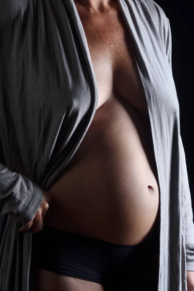 closeup of a pregnant belly with shirt on black background, 6 months,
