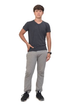 Beyaz arka planda spor giyinmiş genç bir çocuğun tam portresi. Ön manzara ve kalçada eller.