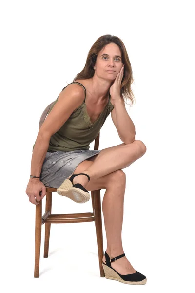 椅子に座って白い背景のカメラを見ているデニムスカートの女性の前に足が交差し — ストック写真