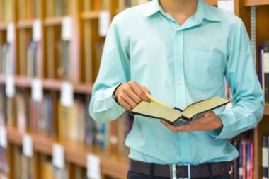 Genç adam kütüphanede kitap okuyor..