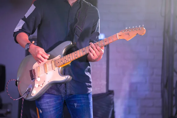 Man playing electric guitar on stage for background with colorful blue and purple scene illumination concept, soft selective focus.