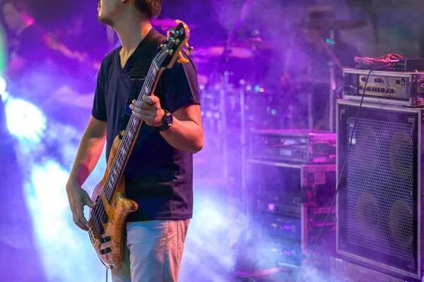 Man playing electric bass guitar on stage for background with colorful blue and purple scene illumination concept, soft selective focus.