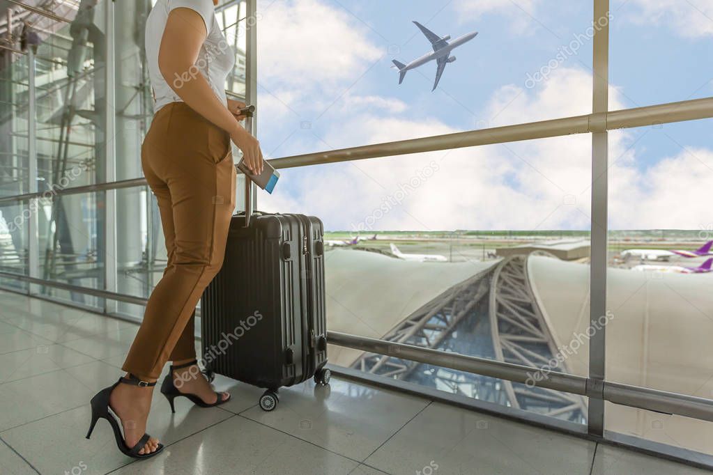 Woman tourist standing with luggage watching sunset at airport window while waiting at boarding gate before departure at lounge. Travel lifestyle.