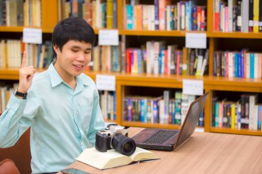 Mutlu başarılı öğrenci zam silah kutluyor kadar gülümseyen çalışması iş projesi bitmiş dizüstü bilgisayar ekranında, kitaplıkta öğrenme genç bakarken.