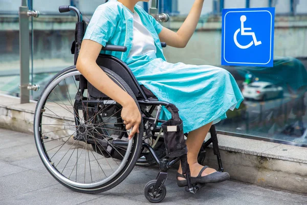 Joven mujer discapacitada en silla de ruedas cerca de señal de pasarela para discapacitados — Foto de Stock
