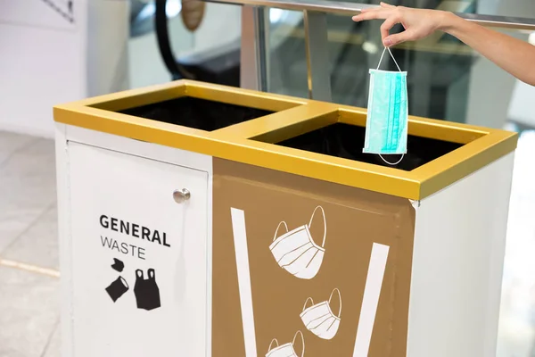 People hand throwing medical face mask into a bin at shopping mall. Right way to protect Coronavirus or Covid-19 concept.