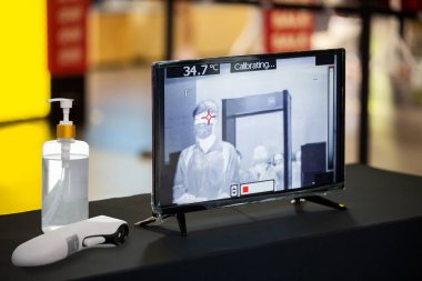 Coronavirus 'un (CoVID-19) vücut ısısını ölçmek için kızılötesi termometre. Alışveriş merkezine girmeden önce kontrol noktasında alkollü el jeli kullanan grip hastası..