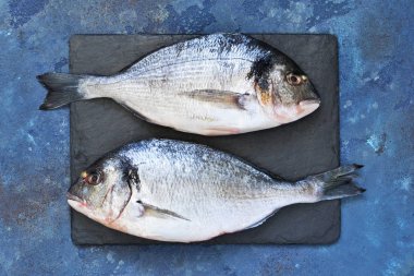 Kuşkonmaz, domates ve baharat bir beton zemin üzerine taze, çiğ Dorado balık. Yemek pişirmek için malzemeler.