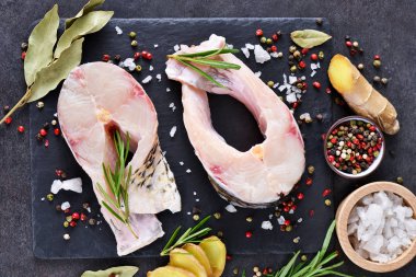 Biftek baharat ve biberiye ile siyah bir taş zemin üzerine beyaz balık.