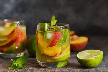Koyu beton arka plan üzerinde şeftali ve kireç ile soğuk limonata.