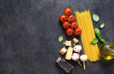 Makarna yapmak için gerekli malzemeler. Siyah arka planda domates ve fesleğenli çiğ spagetti. Yukarıdan görüntüle.