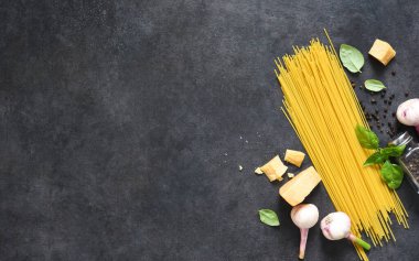 Makarna yapmak için gerekli malzemeler. Siyah arka planda fesleğenli çiğ spagetti. Yukarıdan görüntüle.